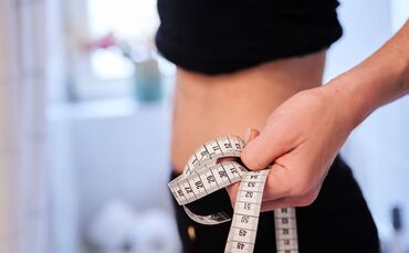 Eine junge Frau hält ein Zentimetermaßband an ihren Bauch