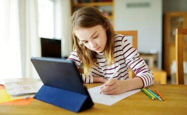 Smart preteen schoolgirl doing her homework with digital tablet at home. Education and distance learning for kids. Homeschooling