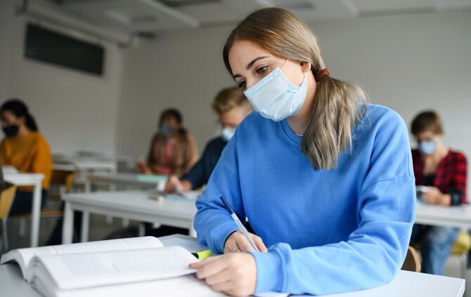 Young students with face masks at desks at college or university, coronavirus concept.
