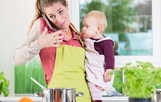 Mother having phone conversation during cooking and holding baby