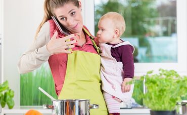 Mother having phone conversation during cooking and holding baby