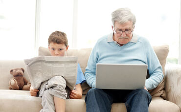 Alter Mann liest am Laptop, Junge liest Zeitung