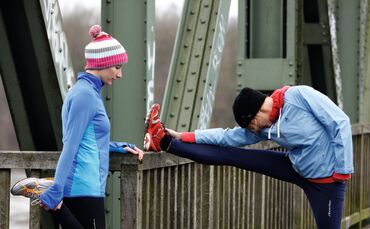 Zwei junge Frauen laufen im Winter, Dehnungsuebungen nach dem Lauf. Joggen in der kalten Jahreszeit, mit waermender, Wind- und Wasserdichter Funktionsbekleidung.