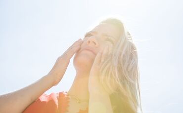 Eine Frau cremt sich mit Sonnencreme das Gesicht ein.