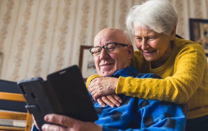 Happy caucasian senior couple smiling and hugging while talking to their children on facetime video chat by using a new smartpho