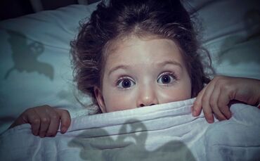 scared cute little girl under the blanket in her bed