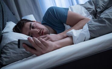 Mann liegt im Bett und schaut auf sein Handy