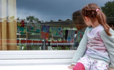 Ein Kind sitzt auf einer Fensterbank.