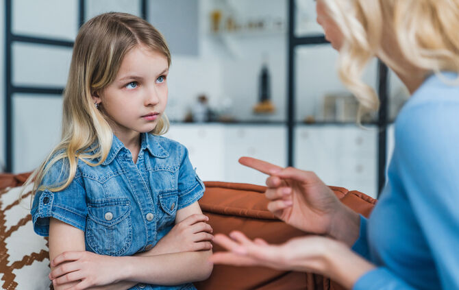 Little girl looking sad while her mother scolding her sitting on couch at home