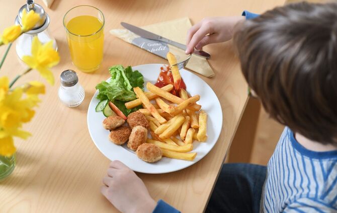 Ein Kind isst Chicken Nuggets und Pommes Frites