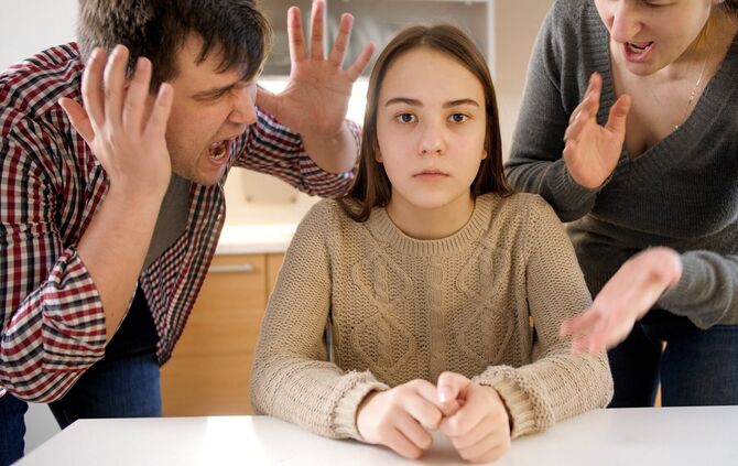 Father and mother shouting and screaming at teenage daughter sitting behind table on kitchen. Family violence, conflicts and rel