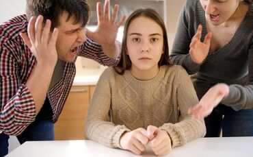 Father and mother shouting and screaming at teenage daughter sitting behind table on kitchen. Family violence, conflicts and rel
