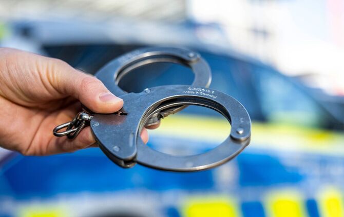 Handschellen vor Polizeiwagen - Symbolbild