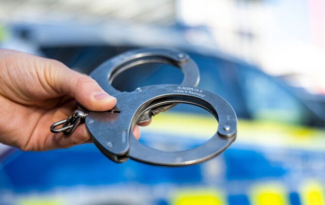 Handschellen vor Polizeiwagen - Symbolbild