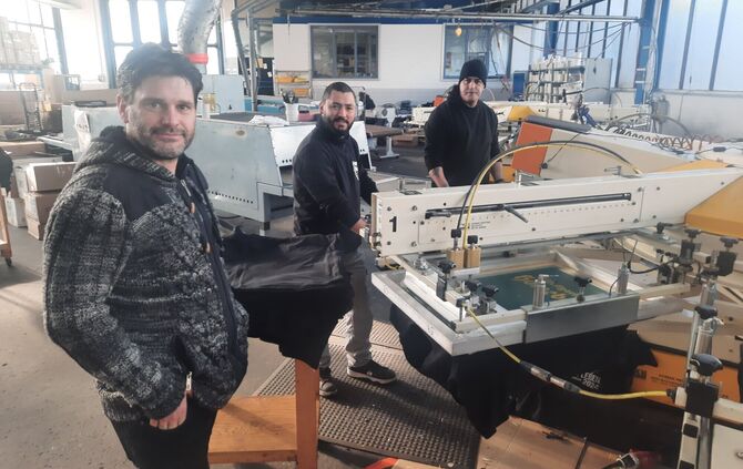 Andreas Kamm mit seinen Angestellten Erhan Demirdas und Fernando Rizzo (von links) an der Textildruckmaschine.