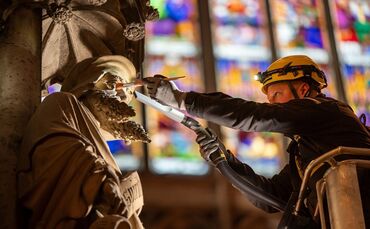 Ein Kärcher-Mitarbeiter entfernt Staub und Kerzenruß von einer Figur im Kölner Dom - in bis zu 43 Metern Höhe.