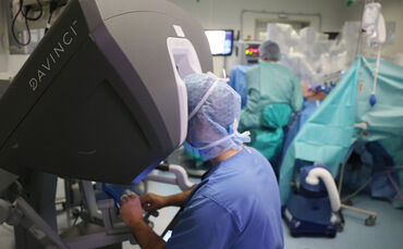 Vorne blickt Dr. Istvan Degrell nach links aufs dreidimensionale DaVinci-Kamerabild aus dem Inneren der Patientin - die Frau, di