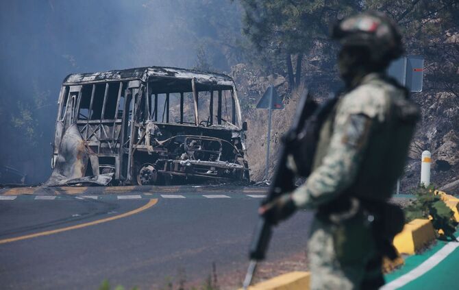 Ein Soldat steht in Cointzio neben einem ausgebrannten Bus