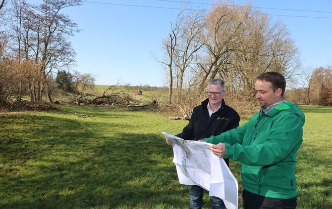 Dezernent Gerd Holzwarth mit Projektleiter Benjamin Kächele (r.). Im Hintergrund die gerodete Fläche am Bach, wo die Brücke hink