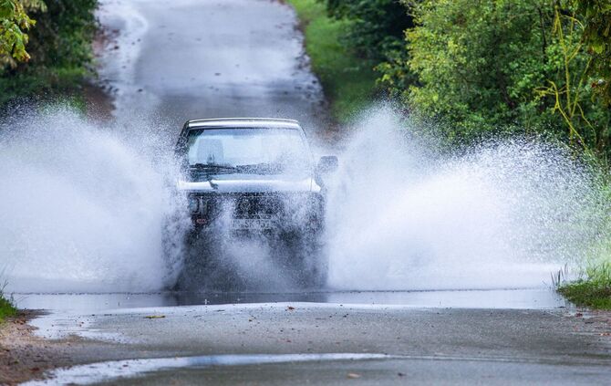 Ein Auto fährt durch eine große Pfütze.