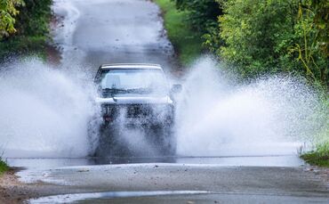Ein Auto fährt durch eine große Pfütze.