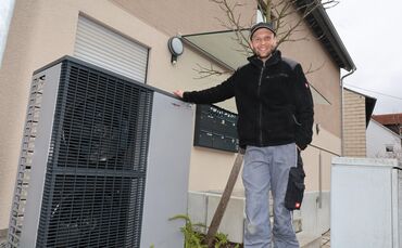 Nico Eifer mit Außengerät der von ihm eingebauten Wärmepumpe an einem Mehrfamilienhaus in Schorndorf.