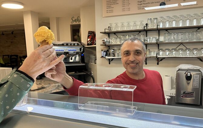 Mohamad Dawara überreicht in der Eisdiele Sahra eine Kugel Mango-Chili-Eis in der Waffel.