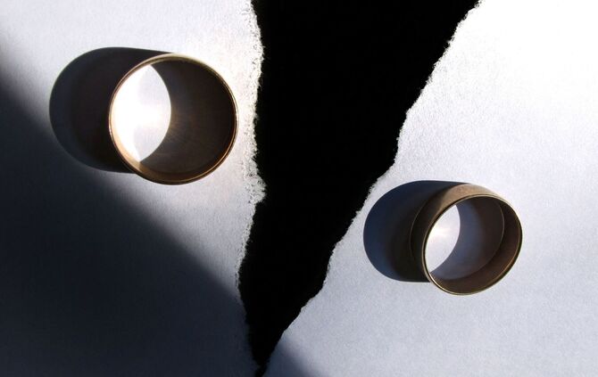 Zwei getragene Eheringe liegen auf einem zerrissenen Papier