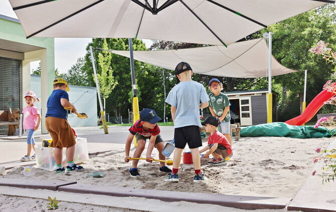 Fleißige Kindergartenkinder im Sandkasten. Besonders wichtig in diesen Tagen: Eine Kappe auf dem Kopf.