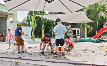 Fleißige Kindergartenkinder im Sandkasten. Besonders wichtig in diesen Tagen: Eine Kappe auf dem Kopf.