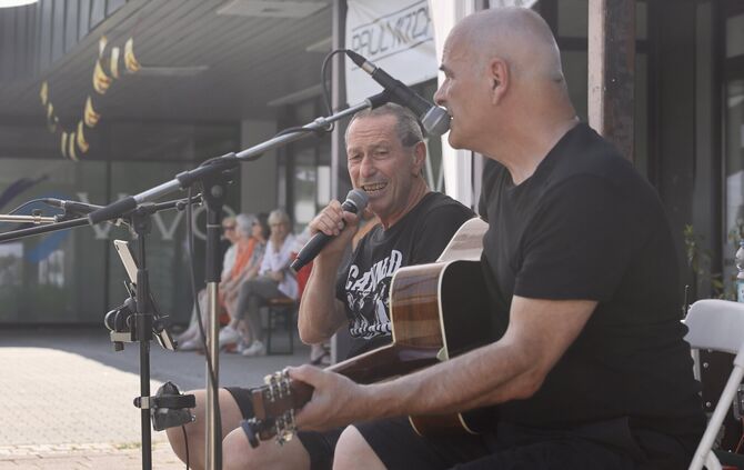 Die Zuhörer haben sich in den Schatten gesetzt, im Vordergrund spielen zwei Musiker der Band: 69 Blue Rd. unter einem Pavillon-D