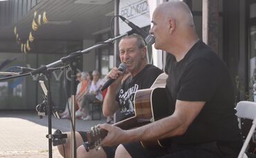 Die Zuhörer haben sich in den Schatten gesetzt, im Vordergrund spielen zwei Musiker der Band: 69 Blue Rd. unter einem Pavillon-D