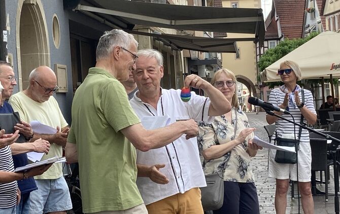 Rupert Kern (grünes Hemd) erhält von Pastor Thomas Mozer ein Regenbogen-Ei. Der Katholik wird die Organisation des Friedensgebet