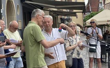 Rupert Kern (grünes Hemd) erhält von Pastor Thomas Mozer ein Regenbogen-Ei. Der Katholik wird die Organisation des Friedensgebet