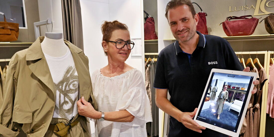 Christian Hartmann, Inhaber von Mode am Markt, zeigt auf dem iPad, wie ein Kleidungsstück aus seinem Geschäft (links) an seiner