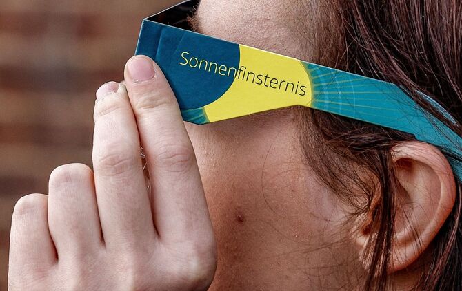 Frau mit Schutzbrille betrachtet eine partielle Sonnenfinsternis
