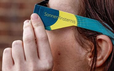 Frau mit Schutzbrille betrachtet eine partielle Sonnenfinsternis
