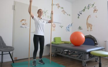 Physiotherapeutin Paulina Trinkle zeigt eine Übung mit Holzstangen, bei der gezielt bestimmte Muskelgruppen angesprochen werden.