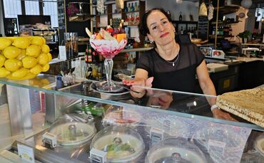 Marisa Bongiovanni steht an der Eistheke mit einem großen Fruchteisbecher. Ihre Eissorten werden in Eismaschinen in der Theke fr