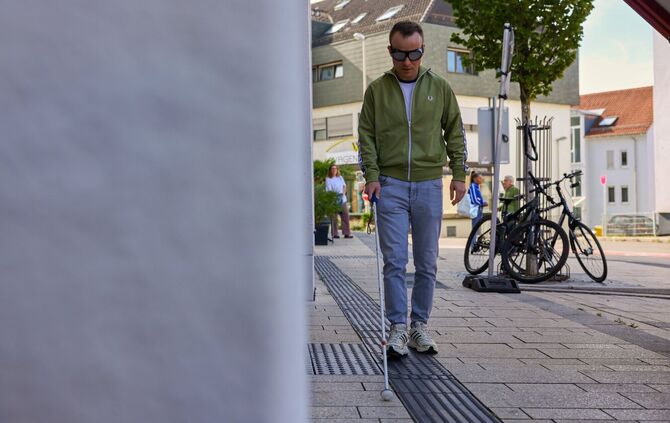 Redakteur Tobias Klecker, ausgestattet mit Blindenstock und einer Brille, die Blindheit simuliert.