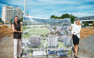 Maklerinnen halten Plakat mit Visualisierung der Neubauten