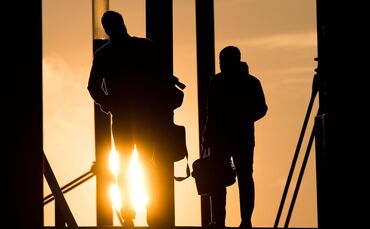 Zwei Männer gehen mit Aktentasche bei Sonnenaufgang über Brücke